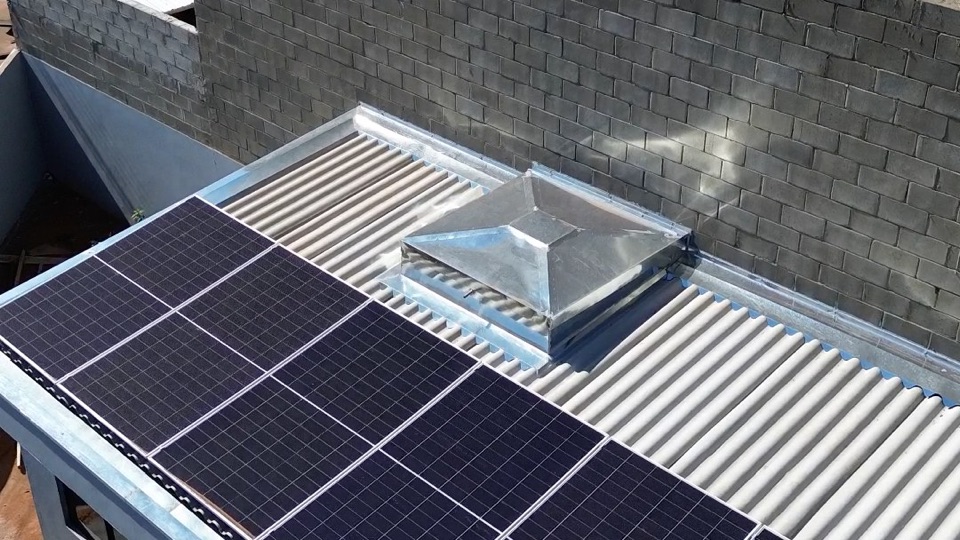 Placas solares em um telhado metálico, ao lado de um galpão, vistas de drone